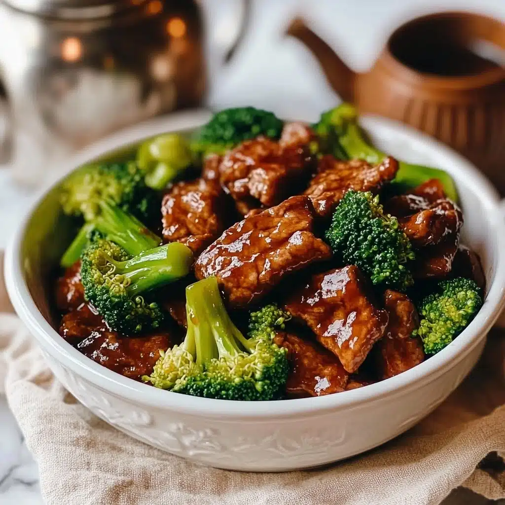 Beef and Broccoli Stir-Fry, homemade Beef and Broccoli, easy Asian stir-fry, quick weeknight dinner, healthy beef stir-fry The image shows a white bowl filled with beef and broccoli stir-fry. The bowl contains a mix of bright green broccoli florets and tender, dark brown pieces of beef coated in a shiny sauce, all layered evenly. The bowl sits on a light beige cloth with a white marbled surface underneath. Nearby, there are wooden chopsticks placed to the right of the bowl and some wrapped fortune cookies. A silver metal teapot is visible at the top left corner.