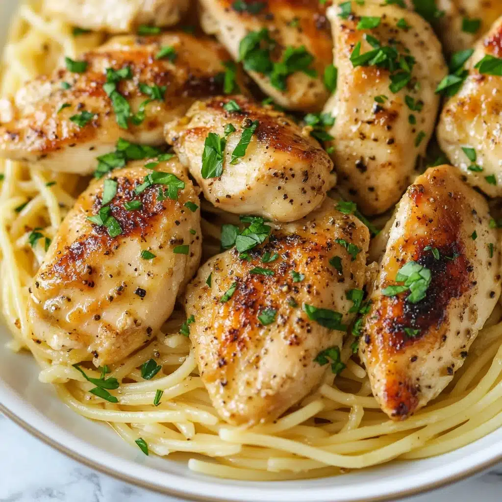 Chicken Scampi Pasta, easy chicken pasta dishes, flavorful garlic lemon pasta, quick weeknight dinner recipes, Italian-inspired chicken pasta The image shows a dish with several pieces of golden-brown cooked chicken placed on a bed of thin spaghetti noodles. The chicken pieces have a slightly crispy texture with visible seasoning and small bits of chopped green herbs and garlic scattered on top. The noodles beneath are pale yellow and look soft, peeking out from under the chicken pieces. The food is served on a white plate, sitting on a white marbled surface.