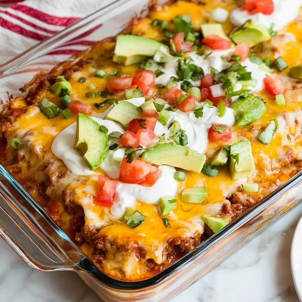 Easy Ground Beef Enchiladas, ground beef enchiladas recipe, cheesy beef enchiladas, quick enchiladas dinner, simple Mexican enchiladas A clear rectangular glass baking dish filled with three layers: the bottom layer is a textured mix of cooked beans and sauce in a brownish-red color, the middle layer is melted yellow cheese covering the entire surface, and the top layer consists of chopped green onions and scattered pieces of melted cheese. On top, there is a long strip of white sour cream spread with diced red tomatoes and light green avocado slices arranged neatly. The dish sits on a white marbled surface with a white cloth with red stripes beside it and a white plate partially visible.