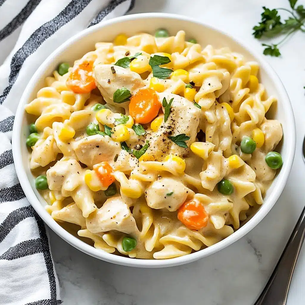Instant Pot Cheesy Chicken, Noodles and Vegetables, Cheesy Chicken and Noodles, Easy Instant Pot Chicken Dinner, Comfort Food Recipes A white bowl filled with creamy pasta made of wide, ruffled noodles mixed with chunks of light-colored cooked chicken, bright green peas, orange diced carrots, yellow sweet corn, and green beans scattered evenly throughout. The dish is garnished with small green herb pieces and some black pepper flakes on top. The bowl is placed on a white marbled surface next to a black and white striped cloth and a silver spoon.
