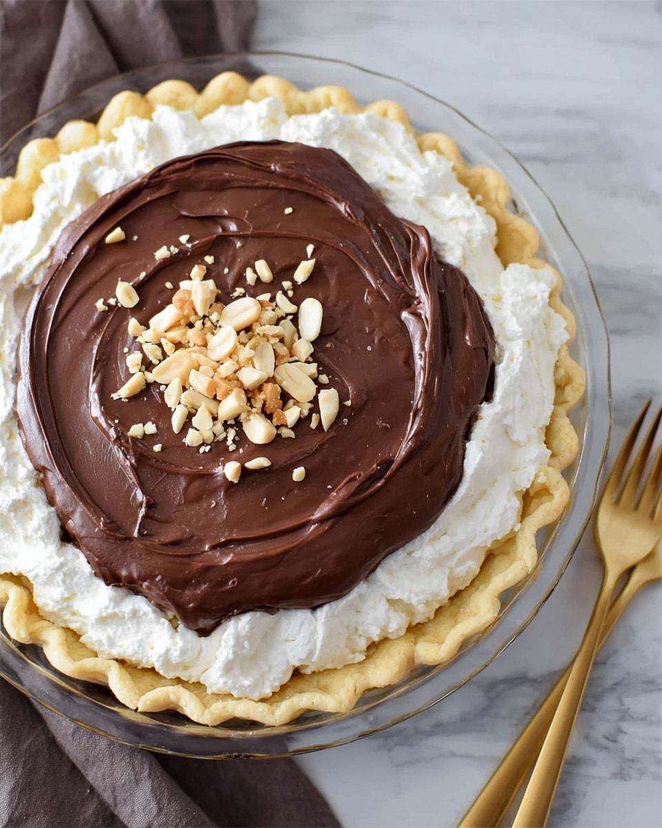 A pie with three layers is shown from above on a clear glass pie dish placed on a white marbled surface. The bottom layer is a pale golden crust with a textured, wavy edge. The middle layer is fluffy and white, looking like whipped cream that is spread thickly and evenly. The top layer is a smooth, dark chocolate pudding or ganache, spread thick and swirled softly. In the center of the chocolate layer, there is a small pile of chopped light beige and white nuts, adding texture and color contrast. A gold fork lies beside the pie on the surface. Photo taken with an iphone --ar 4:5 --v 7