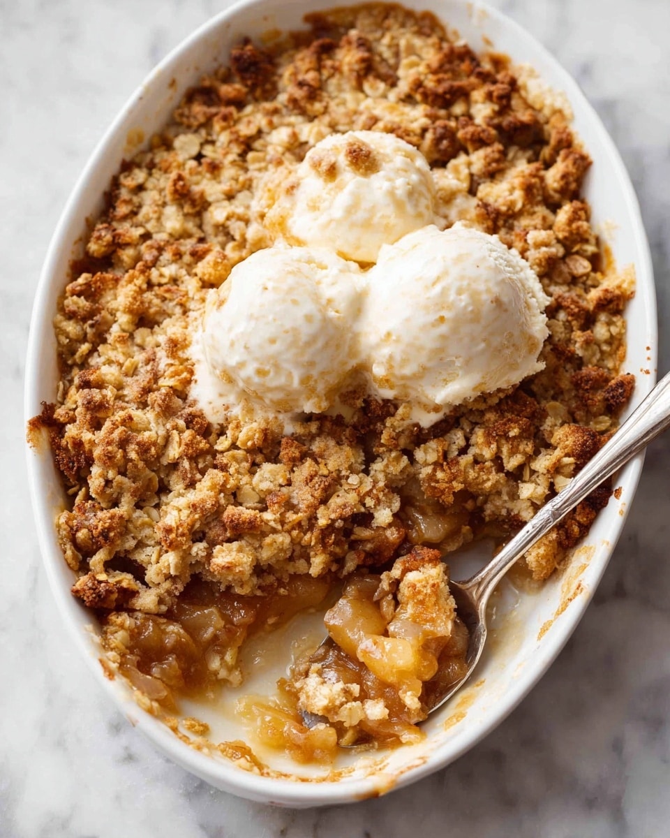 The image shows a white oval baking dish filled with a two-layer dessert. The bottom layer is a soft, cooked fruit mix that is light brown and slightly translucent, with a juicy texture. The top layer is a thick, crumbly oat topping that is golden brown with some darker toasted bits, creating a rough, crunchy surface. Two scoops of melting vanilla ice cream rest on top, adding a smooth, creamy white contrast. A spoon with some of the fruit and oat topping scooped up is near the bottom right of the dish. The dish is placed on a white marbled surface. photo taken with an iphone --ar 4:5 --v 7