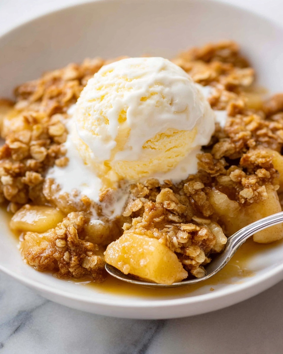 The dish is apple crisp served in a white bowl placed on a white marbled surface. The base layer consists of tender, warm apple chunks with a light golden color, slightly soft and coated in syrup. On top, there is a thick layer of golden brown oat crumble with a rough, crumbly texture. Centered on the crumble is a single scoop of smooth, creamy vanilla ice cream, beginning to melt and blend into the warm crisp below. A silver spoon is scooping from the side. Photo taken with an iphone --ar 4:5 --v 7