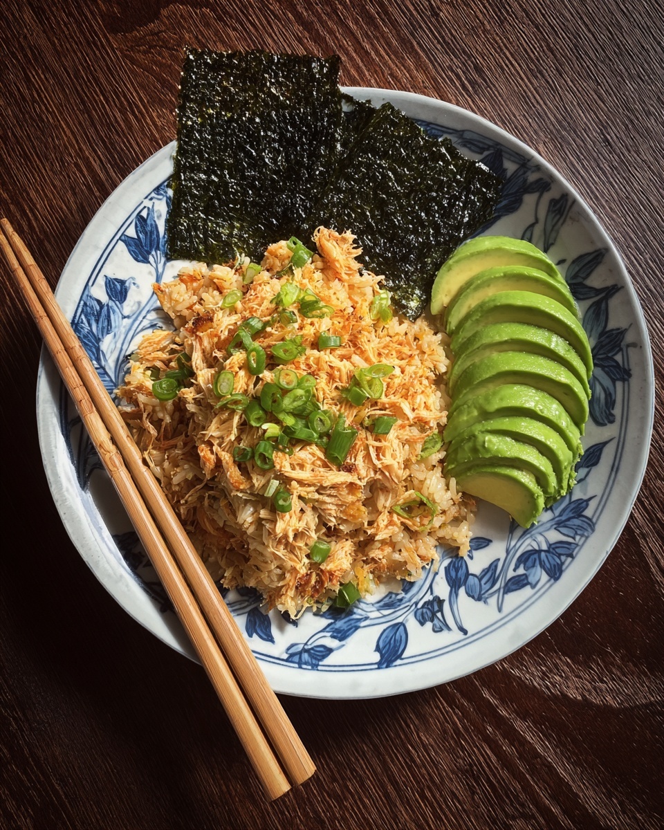 The dish shows a white plate with a blue leaf pattern filled with seasoned rice mixed with shredded orange fish and topped with chopped green onions, sitting on a dark wooden surface. To the right side of the rice is a neat fan-shaped layer of bright green avocado slices, next to a dark, shiny seaweed square resting on the edge of the plate. Two light wooden chopsticks rest on the left side of the plate. Photo taken with an iphone --ar 4:5 --v 7