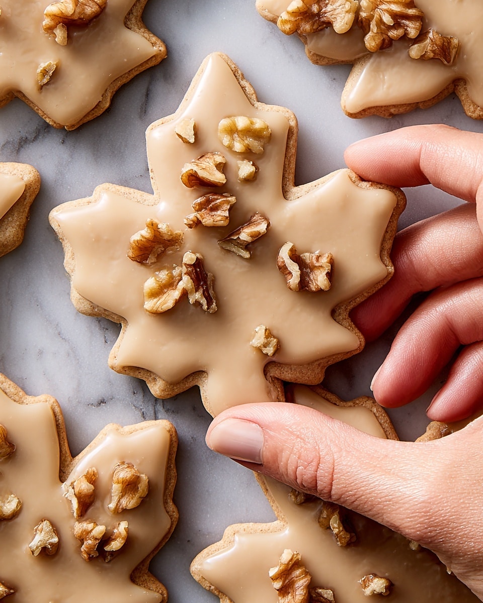 Several maple leaf shaped cookies are spread out on a white marbled surface. Each cookie has one layer, covered with smooth light brown icing that has a glossy texture. On some cookies, one side is decorated with small chunks of chopped walnuts, adding a rough and crunchy detail. The cookies are closely placed but not overlapping. photo taken with an iphone --ar 4:5 --v 7