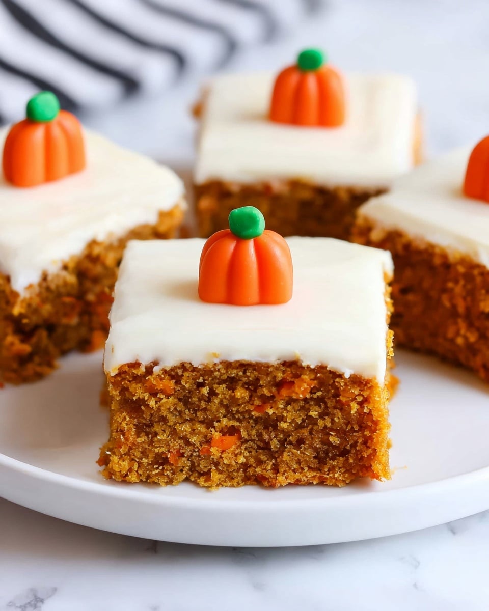 The image shows square pieces of moist carrot cake with two visible layers: the bottom layer is a textured orange-brown cake, and the top layer is smooth white frosting. Each piece is decorated in the center with a small, bright orange candy shaped like a pumpkin with a green stem. The cake squares are placed on a white plate, set against a white marbled surface. Photo taken with an iphone --ar 4:5 --v 7