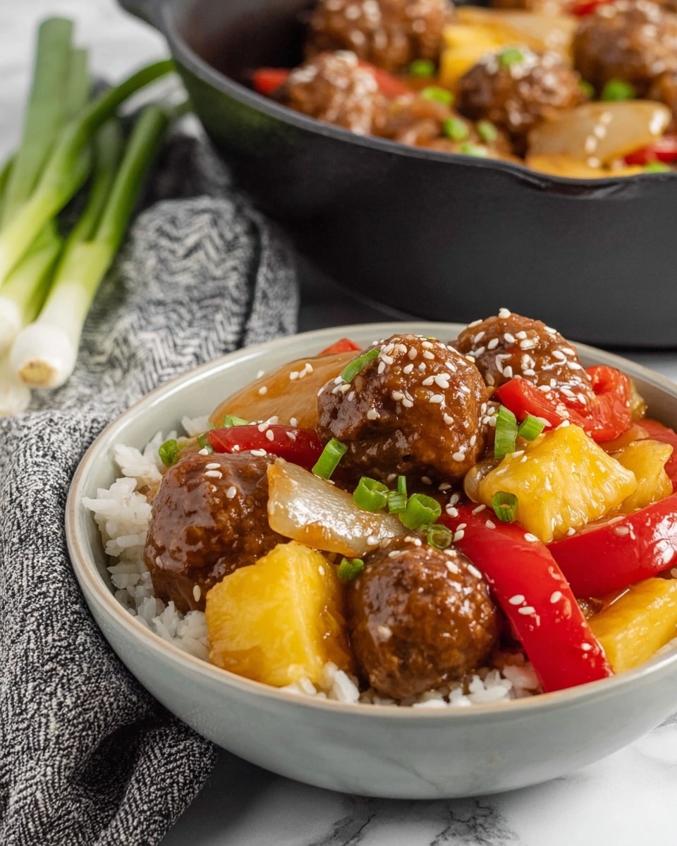 The image shows a white bowl filled with three main layers: a bottom layer of white rice, a middle layer of mixed vegetables with yellow pineapple chunks, red bell pepper pieces, and translucent cooked onions, and a top layer of brown meatballs covered in a shiny brown sauce sprinkled with white sesame seeds. Behind the bowl, there is a black cast iron pan with similar contents and some green onions lying on a cloth with a gray and white pattern. The surface under everything is white marble. photo taken with an iphone --ar 4:5 --v 7