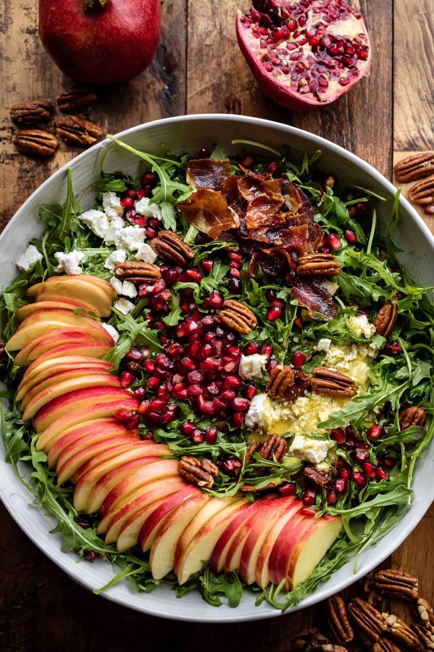 A large white bowl filled with a colorful salad resting on a wooden surface. The base layer is fresh green arugula leaves spread evenly, topped with neatly sliced red and light yellow apples arranged in fanned clusters scattered throughout. Small bits of white cheese are sprinkled over the salad, adding contrast. There are dark red pomegranate seeds dotted across the salad, mixed with toasted nuts that add a crunchy texture and deep brown color. Pieces of crispy, thin slices of brown bacon or prosciutto are interspersed, giving extra warmth to the colors. Two wooden salad spoons with smooth handles rest inside the bowl on opposite sides. In the background, half a pomegranate with bright red seeds is on a white plate, along with small bunches of fresh green herbs and a few stray nuts. The whole scene is against a white marbled texture. photo taken with an iphone --ar 2:3 --v 7 - Autumn Harvest Honeycrisp Apple and Feta Salad, fall apple salad, honeycrisp apple salad, autumn fruit salad, easy fall salad recipes