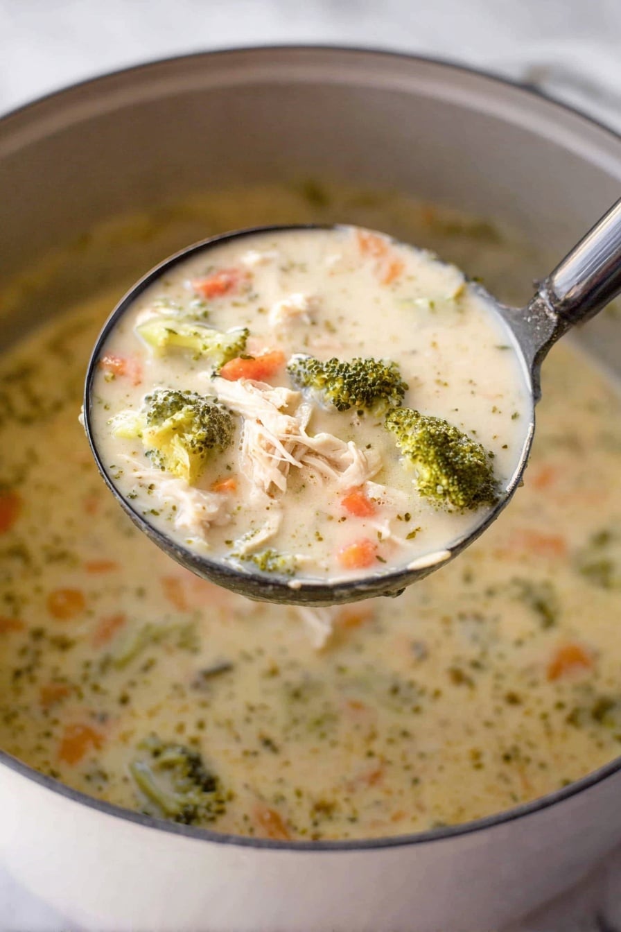 A close-up shot shows a ladle filled with creamy chicken and broccoli soup held above a pot. The soup has a thick, creamy texture with visible chunks of light beige shredded chicken, bright green broccoli florets, and small orange carrot pieces mixed throughout the light cream-colored broth. The surface beneath the pot is a white marbled texture. Photo taken with an iphone --ar 2:3 --v 7 - Creamy Chicken and Broccoli Soup, chicken broccoli soup, creamy chicken soup, healthy chicken soup, comforting soup recipes