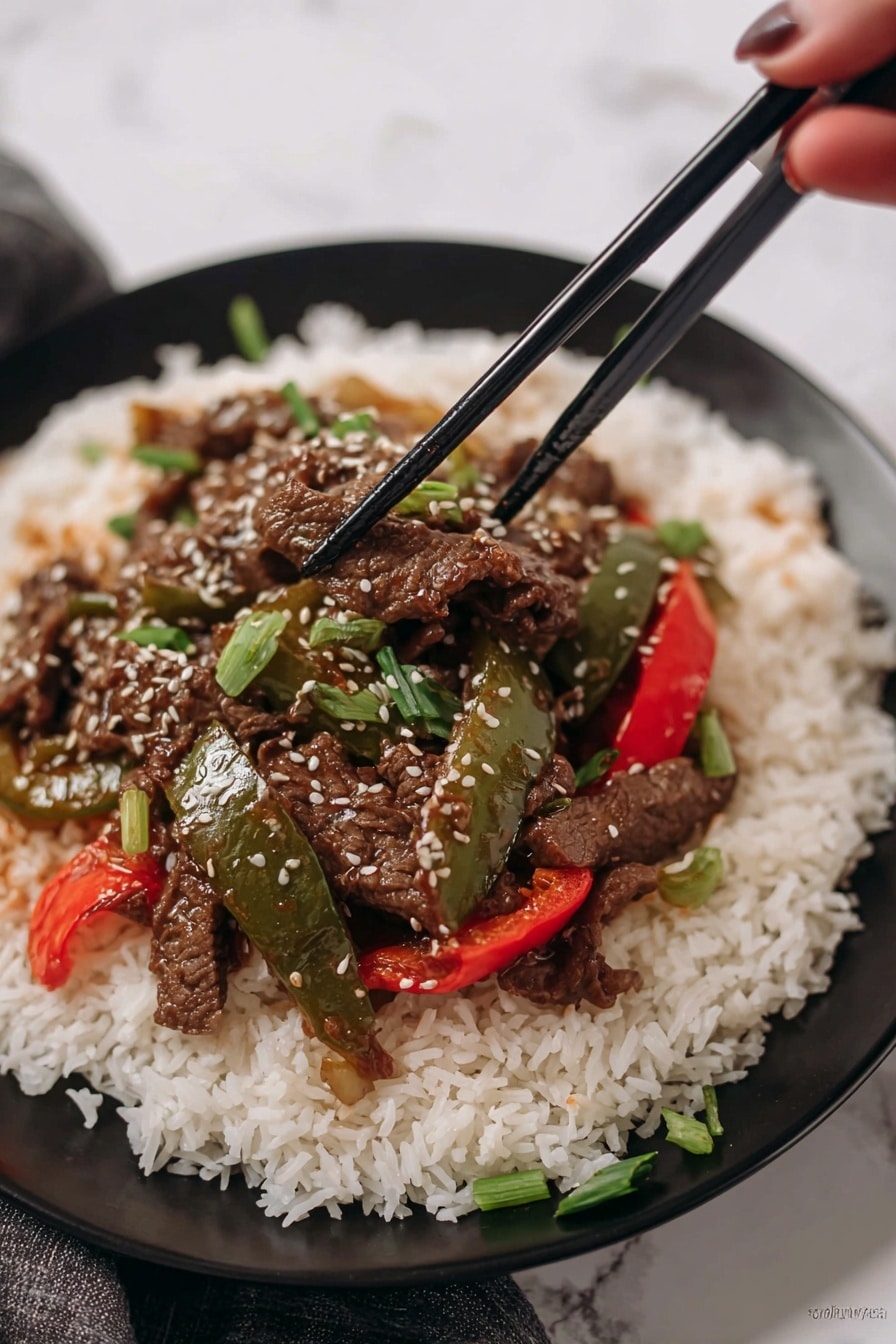 A white plate holds a large base layer of fluffy, long-grain white rice, spread evenly across the plate. On top of the rice sits a colorful stir-fry with three distinct elements: dark brown thin strips of cooked beef, glossy green bell pepper slices, and bright red bell pepper slices. The stir-fry is sprinkled with small white sesame seeds and chopped green onion pieces for freshness. Two black chopsticks rest across the top edge of the plate. The background shows a red bell pepper and green leafy herbs on a white marbled surface. Photo taken with an iphone --ar 2:3 --v 7 - Crockpot Pepper Steak, easy slow cooker beef dinner, tender beef and peppers recipe, savory crockpot beef, quick comfort food dinner