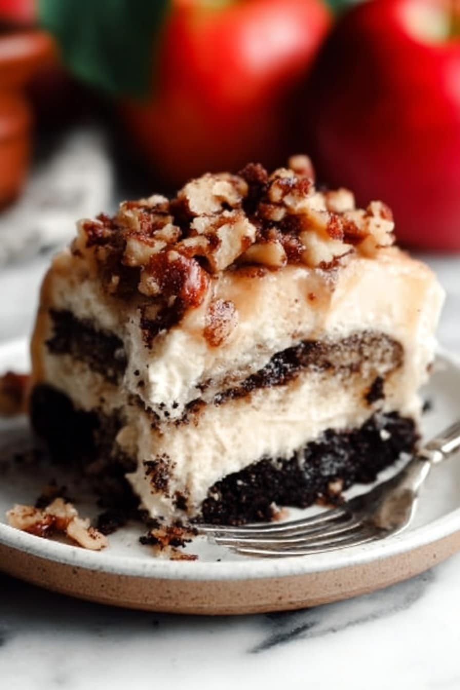 The image shows a close-up of a thick slice of layered dessert on a white plate. The bottom layer is dark and crumbly, looking like crushed chocolate cookies. Above that, there is a creamy, light beige layer that looks soft and smooth. On top, there is a sprinkle of chopped nuts mixed with small crumb pieces, giving a crunchy texture. A metal fork rests on the plate near the dessert. The background has a white marbled surface, and there are whole red apples blurred in the background. Photo taken with an iphone --ar 2:3 --v 7 - Apple Pie Cinnamon Rolls with Apple Cider Caramel Sauce and Cream Cheese Frosting, apple cinnamon roll recipe, fall dessert recipes, cinnamon rolls with caramel, apple pie flavored baked goods