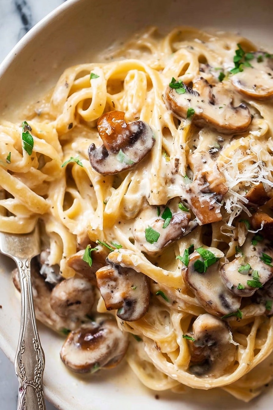 A close-up of creamy pasta with several long, flat noodles twisted and layered, covered in a smooth, off-white sauce. On top and mixed into the pasta are many thin slices of cooked mushrooms with a light brown color and soft texture. Small pieces of fresh green herbs are scattered over the whole dish, adding a splash of color. The dish is on a white plate with a fork partially wrapped in the pasta at the bottom left corner. The background is a white marbled texture. Photo taken with an iphone --ar 2:3 --v 7 - Creamy Mushroom Pasta, easy mushroom pasta, quick mushroom pasta dinner, homemade mushroom pasta, comfort food mushroom pasta