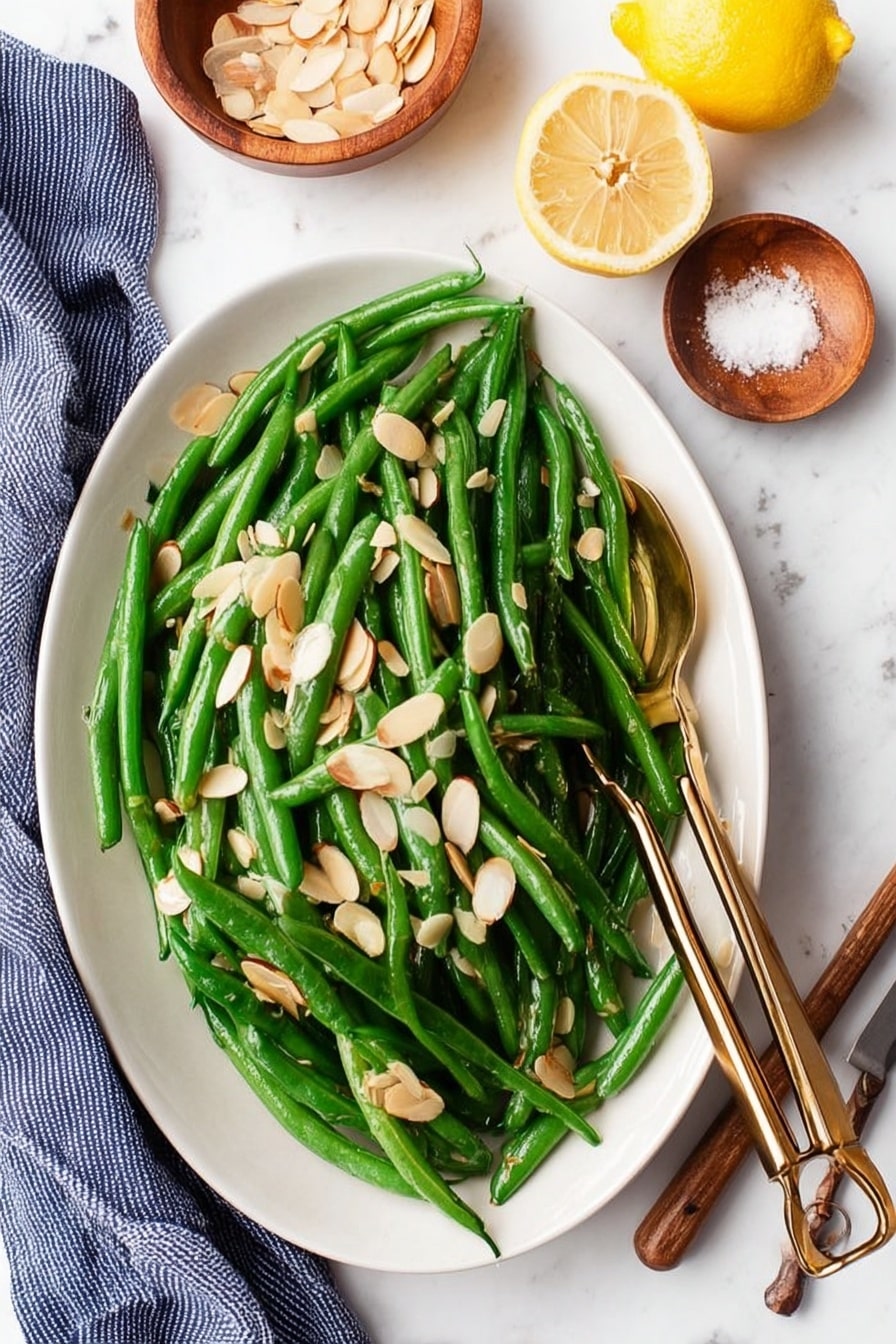 A close-up view of a black cast iron skillet filled with bright green cooked green beans mixed with thin slices of cooked white onions. A light-colored wooden spatula with visible grain rests on top of the green beans, placed in the center of the skillet. The skillet sits on a white marbled surface with a light gray cloth partially visible behind it. To the upper right, there is a wooden spoon holding two halves of a yellow lemon. At the bottom of the image, two small wooden objects are slightly visible. The whole scene has soft, natural light highlighting the fresh textures. photo taken with an iphone --ar 2:3 --v 7 - Green Beans Almondine, easy green bean side dish, almond green beans, lemon green beans recipe, quick vegetable side