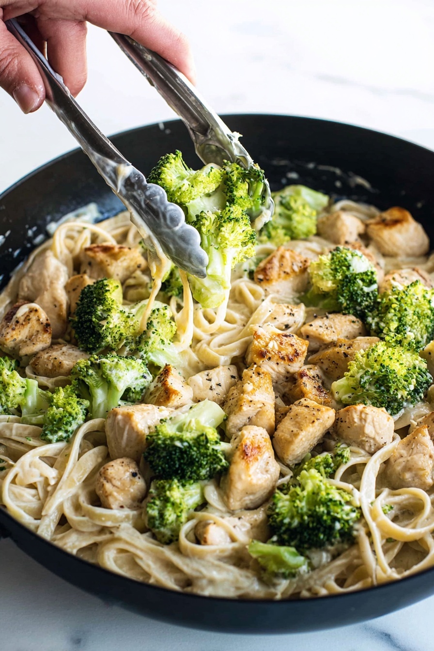A close-up view of a black pan filled with creamy pasta layered at the bottom in a pale beige color with smooth texture. On top, there are chunks of cooked chicken pieces, golden brown with light black pepper spots, scattered evenly. Bright green broccoli florets, fresh and slightly steamed, are spread over the chicken and pasta. A woman's hand holding silver tongs with white sauce spots is seen in the upper right, picking up some broccoli and chicken. The background is a white marbled texture. photo taken with an iphone --ar 2:3 --v 7 - Creamy Chicken Broccoli Fettuccine, easy creamy pasta, quick chicken and broccoli pasta, comforting weeknight dinner, homemade Alfredo pasta