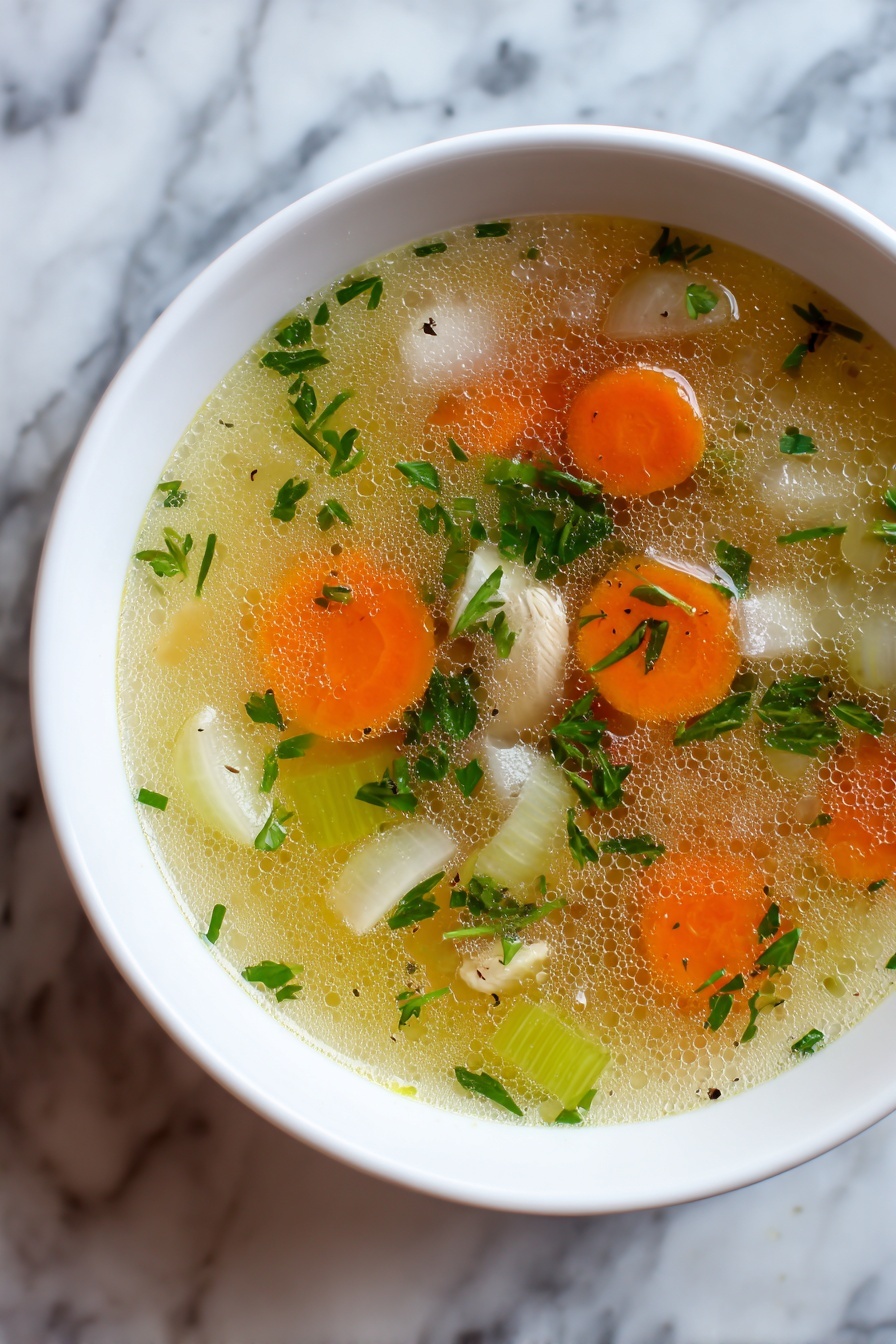 A white bowl filled with clear chicken soup on a white plate, showing three layers: a top layer of clear golden broth with small oil drops, a middle layer with soft shredded chicken pieces in cream color mixed with green leafy vegetables and small orange carrot cubes, and a bottom layer of translucent broth with small green peas and herbs. The bowl is placed on a white marbled surface with a spoon on the right side. Photo taken with an iphone --ar 2:3 --v 7 - Mom's Cold-Season Chicken Soup, winter chicken soup, comforting chicken broth, homemade chicken soup recipe, cozy chicken soup ideas