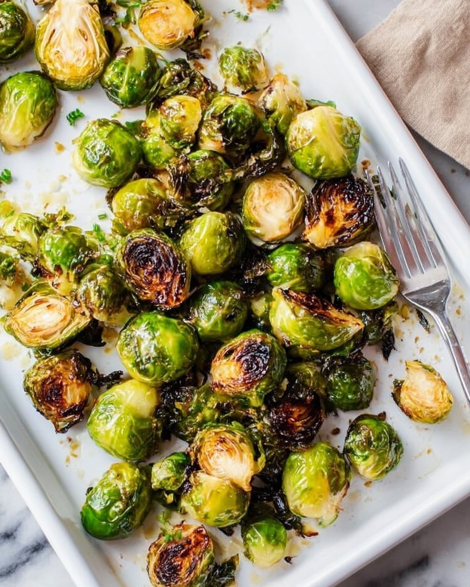 A white tray filled with roasted Brussels sprouts, some whole and some halved, all showing a mix of bright green and dark brown charred spots, creating a crispy texture on the outside. The sprouts have a slightly glossy look from oil and are spread unevenly over the tray, with some pieces clustered near the edges. A silver fork is placed on the right side of the tray, partially under some sprouts. The background surface is a white marbled texture. Photo taken with an iphone --ar 4:5 --v 7
