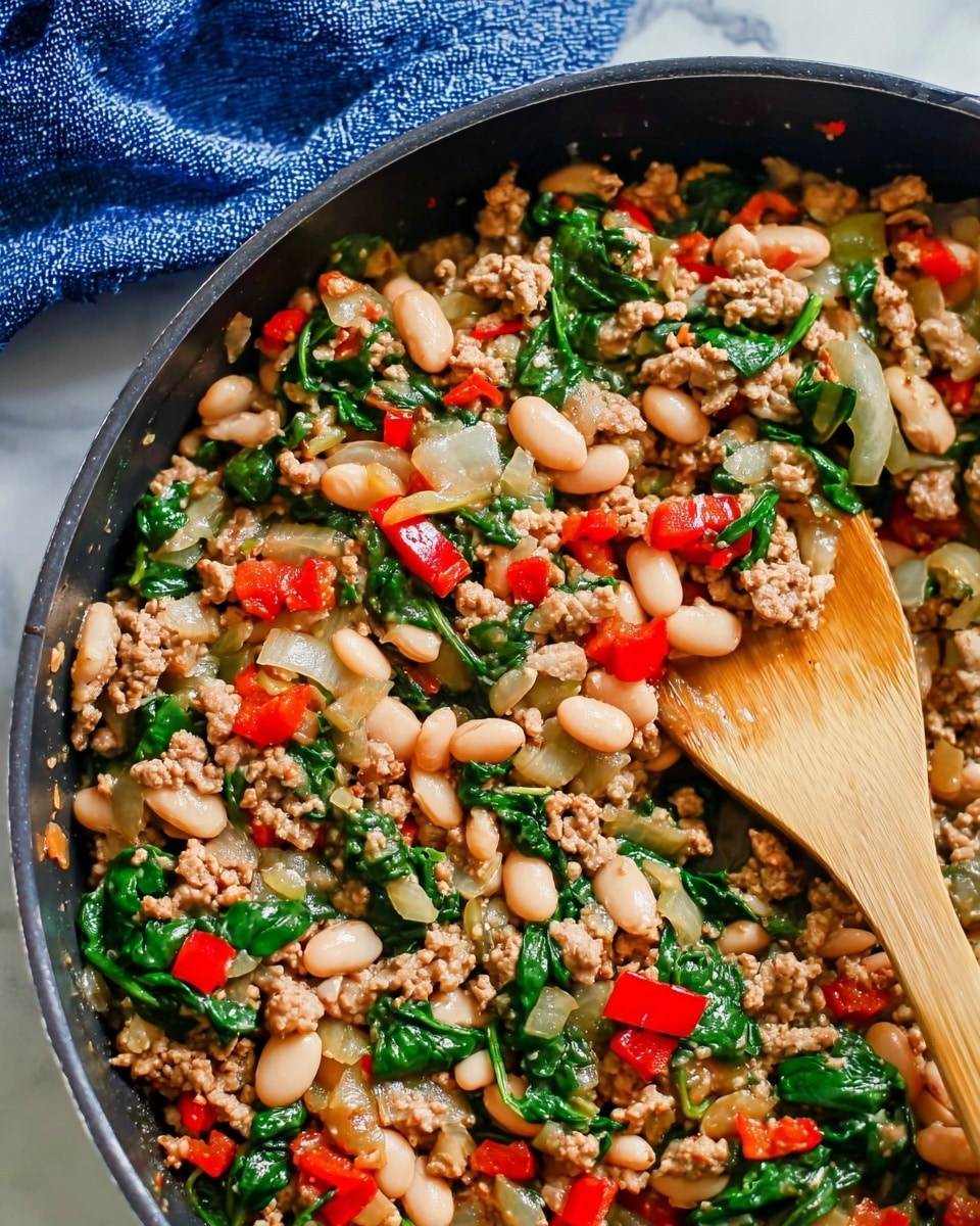 A close-up view of a cooked dish in a deep, black pan showing a mix of four layers. The bottom layer is green spinach leaves with a shiny texture, spread evenly. Above it is a layer of white beans that are smooth and oval-shaped, scattered throughout. The next layer consists of small pieces of cooked ground meat in light brown, mixed evenly all over. The top layer includes diced red and green bell peppers and translucent white onions, creating pops of bright colors. A wooden spoon with a smooth light brown surface rests on the right side of the pan. The scene is set on a white marbled surface with a blue cloth in the background. photo taken with an iphone --ar 4:5 --v 7