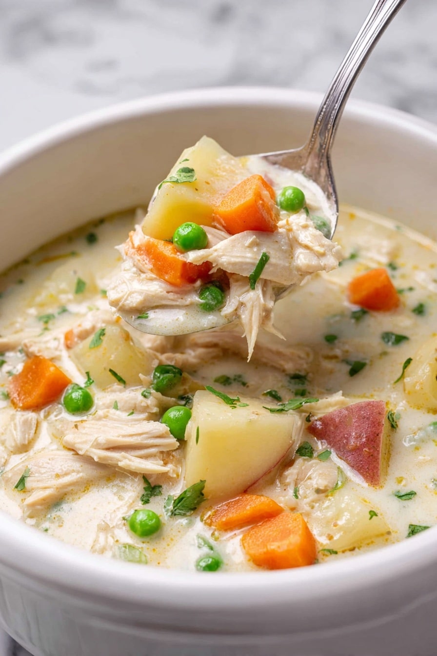 A white bowl filled with thick creamy chicken soup shows several layers: the base is a light cream broth, with chunks of light beige shredded chicken, bright orange carrot slices, small green peas, and white potato pieces with reddish skin. A silver spoon lifts a scoop of the soup, filled with all these colorful ingredients, positioned slightly above the bowl. The background is a white marbled texture, giving a clean and fresh look to the image. Photo taken with an iphone --ar 2:3 --v 7 - Slow Cooker Garlic Parmesan Chicken Stew, creamy chicken stew, easy slow cooker dinner, hearty chicken and veggie stew, comfort food recipes