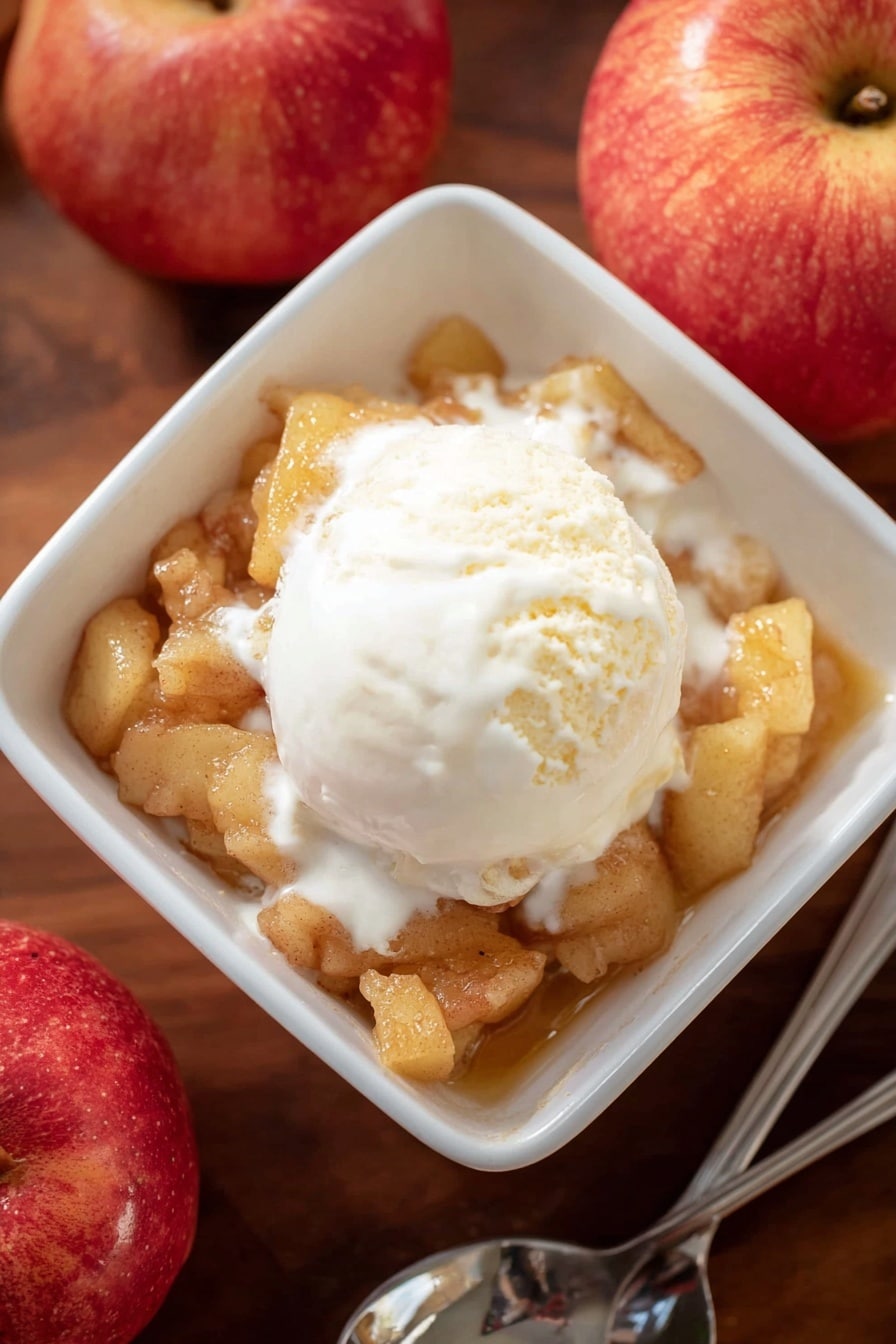 A white square bowl is filled with one layer of soft cooked apple pieces with a light brown color and chunky texture. On top, there is one scoop of creamy white vanilla ice cream that is melting slightly, spreading smooth white cream over the apples. The bowl sits on a wooden surface next to two red apples and a silver spoon. The lighting is soft and natural, highlighting the warm and cool tones of the dessert. photo taken with an iphone --ar 2:3 --v 7 - Apple Brown Betty, Apple Brown Betty dessert, fall dessert recipes, easy apple crumble, cozy apple dessert