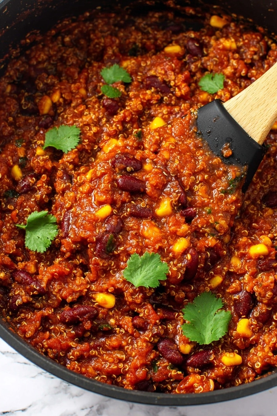 The image shows a thick, rich mixture in a black pan filled with three main layers: grains that look like tiny beige quinoa, dark red kidney beans, and bright yellow corn kernels, all mixed with a deep red tomato-based sauce. The texture is chunky with small bits of vegetables and beans visible throughout. There are several fresh green cilantro leaves scattered on top for contrast. A wooden spoon with a black silicone head is scooping some of the mixture from the pan. The background is a white marbled texture. Photo taken with an iphone --ar 2:3 --v 7 - Slow Cooker Vegan Bean & Quinoa Chili, vegan chili recipe, plant-based slow cooker chili, healthy vegan chili, hearty vegan chili