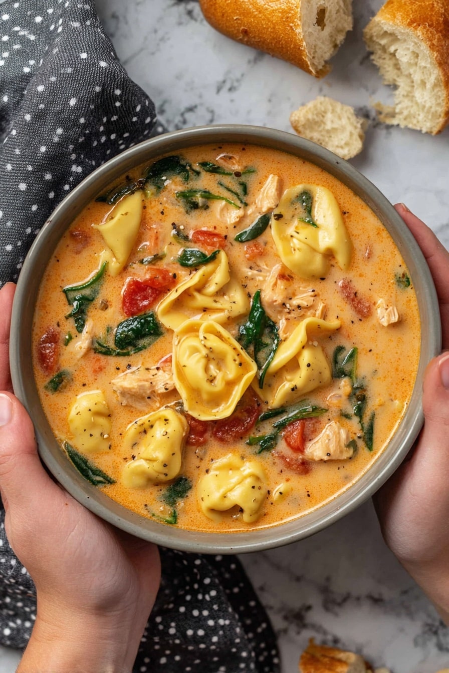 A black slow cooker filled with creamy orange soup containing plump yellow tortellini pasta, scattered fresh dark green spinach leaves, and small red tomato pieces mixed in a smooth sauce with visible bits of white shredded chicken, a curved wooden spoon resting inside the cooker, placed on a white marbled surface with pieces of toasted bread on a gray cloth nearby photo taken with an iphone --ar 2:3 --v 7 - Creamy Crock Pot Chicken Tortellini Soup, slow cooker chicken tortellini soup, cheesy chicken tortellini stew, easy chicken tortellini soup, comforting slow cooker soup