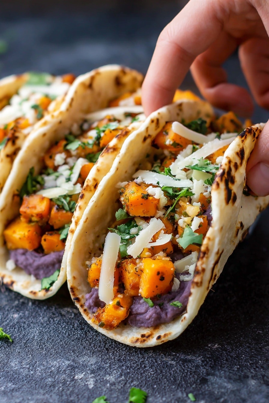 The image shows three small tacos placed closely side by side on a dark textured surface. Each taco has three layers: the bottom layer is a white corn tortilla with light brown spots from cooking, the middle layer is mashed purple beans spread evenly, the top layer consists of bright orange cubes of cooked squash mixed with small green cilantro leaves, and thin pale white strips of cheese scattered on top. A woman's hand is gently holding the front taco, lifting the tortilla slightly to reveal the filling inside. Photo taken with an iphone --ar 2:3 --v 7 - Black Bean Sweet Potato Tacos, vegetarian taco recipes, healthy taco ideas, meatless dinner recipes, easy vegan tacos