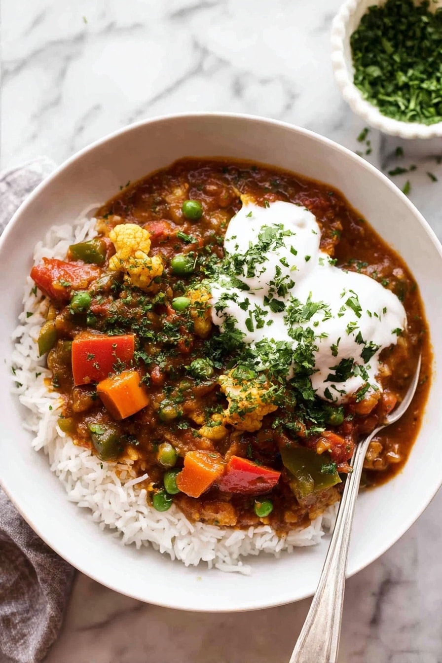 A white bowl filled with a base layer of white rice topped with a colorful vegetable curry. The curry has pieces of orange carrots, bright green peas, red bell peppers, and bits of cauliflower all mixed in a rich reddish-brown sauce. On top of the curry, there are two dollops of smooth white yogurt sprinkled with chopped green herbs. A silver spoon rests inside the bowl on the right side. The bowl is placed on a white marbled surface, and in the background, there is a small white bowl filled with chopped green herbs. photo taken with an iphone --ar 2:3 --v 7 - Vegetable Curry, Healthy Vegetable Curry, Vegan Vegetable Curry, Easy Vegetable Curry, Wholesome Vegetable Curry