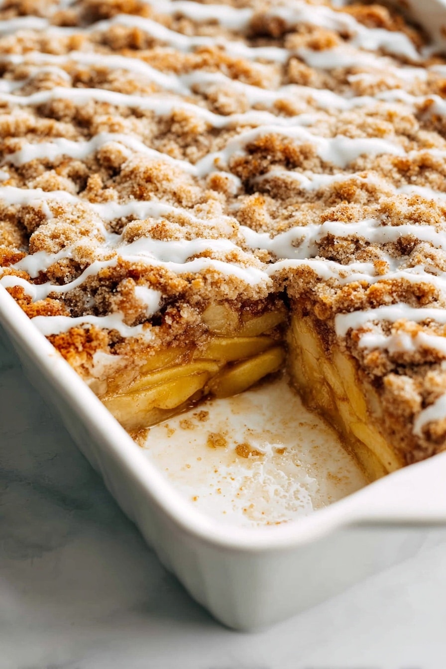 A white baking dish holds a multi-layered baked dessert with three visible layers. The bottom layer is made of soft cooked apple slices, pale yellow in color, resting on a thin, golden crust. Above this, there is a thick, light brown crumbly streusel layer that looks crunchy and uneven, covering the apples. A thin, slightly shiny drizzle of white icing runs lightly across the top streusel layer in wavy lines. The edges of the dish show some baked-on residue, adding a homemade feel. The white marbled surface beneath the dish adds a clean, bright background. photo taken with an iphone --ar 2:3 --v 7 - Apple French Toast Casserole, baked apple breakfast, cinnamon apple brunch, easy apple casserole, cozy breakfast recipes