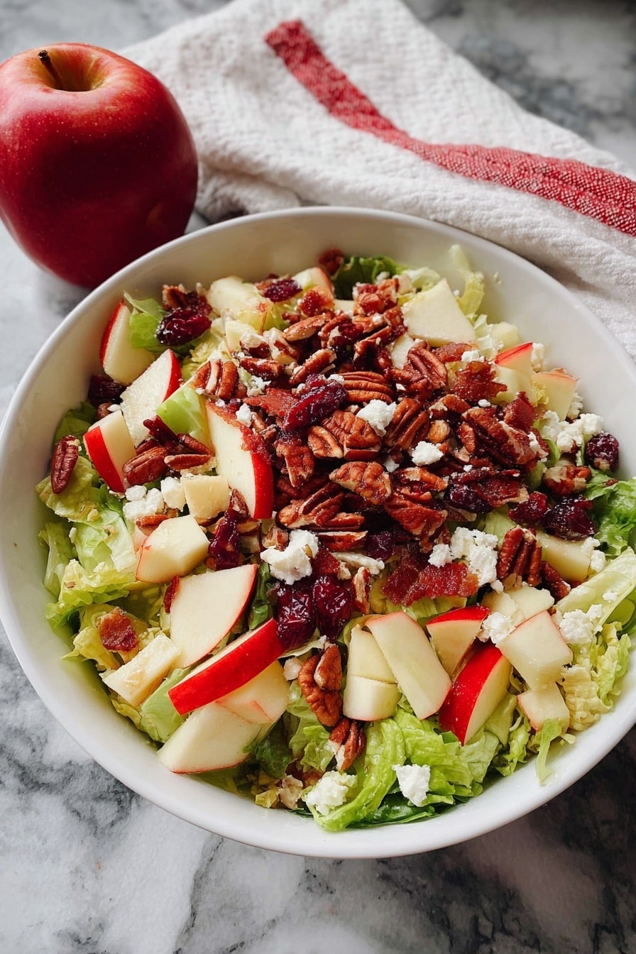 A white bowl holds a fresh salad with three main layers. The bottom layer is a mix of green lettuce leaves, light and crispy in texture. On top of the lettuce, there are chopped red and green apple pieces with smooth skin and crunchy texture. Scattered all over the apples and lettuce are small white crumbles of cheese and reddish dried cranberries. The top layer is made up of pecan nuts, brown and slightly rough, spread evenly across the surface. The bowl sits on a white marbled surface, next to a red apple and a white cloth with red stripes. Photo taken with an iphone --ar 2:3 --v 7 - Honeycrisp Harvest Salad, autumn apple salad, maple bacon salad, apple cider vinaigrette salad, easy fall salad recipes