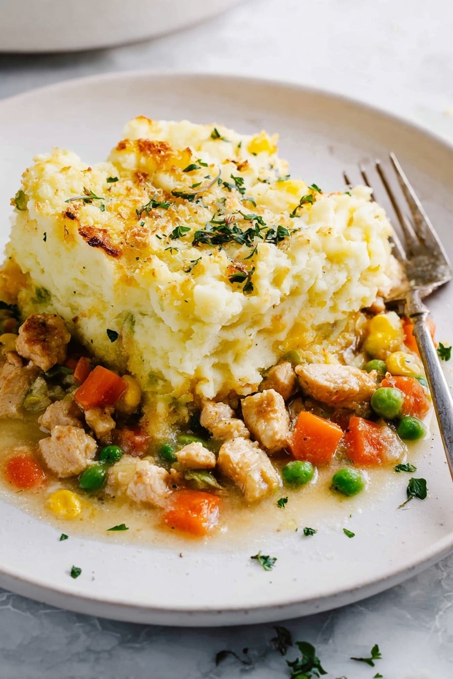 The dish shows two layers on a white plate with a white marbled surface below. The bottom layer is a mix of small pieces of light brown cooked chicken, bright orange carrot cubes, green peas, and some yellow bits, all in a light sauce. The top layer is a thick, fluffy heap of mashed potatoes with a pale yellow color and a slightly browned, baked texture on the edges. Small green herb pieces are sprinkled over the top and around the plate. A metal fork rests on the right side of the plate. photo taken with an iphone --ar 2:3 --v 7 - Healthy Turkey Shepherd's Pie, Turkey Shepherd's Pie, Healthy Shepherd's Pie, Light Shepherd's Pie, Nourishing Turkey Shepherd's Pie
