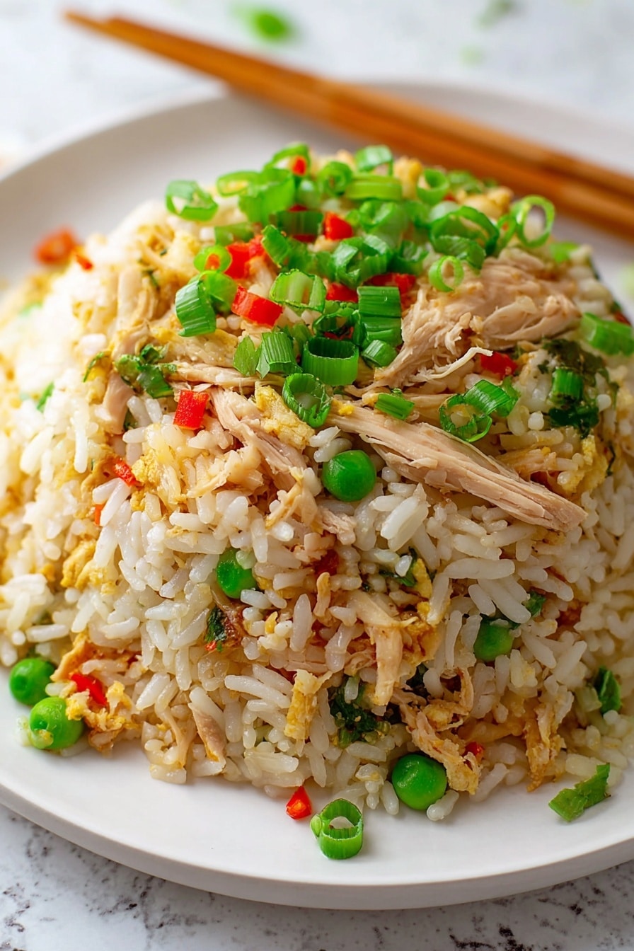 A close-up view of a mound of fried rice on a white plate, placed on a white marbled surface. The dish has three main layers: the bottom layer is white and slightly golden rice grains, the middle layer contains shredded light brown chicken pieces mixed with small green peas, and the top layer is scattered with bright green chopped spring onions and tiny red bell pepper bits. Wooden chopsticks rest diagonally at the back of the plate. Photo taken with an iphone --ar 2:3 --v 7 - Quick Chicken Fried Rice, chicken fried rice, easy fried rice recipe, quick dinner ideas, homemade Asian fried rice