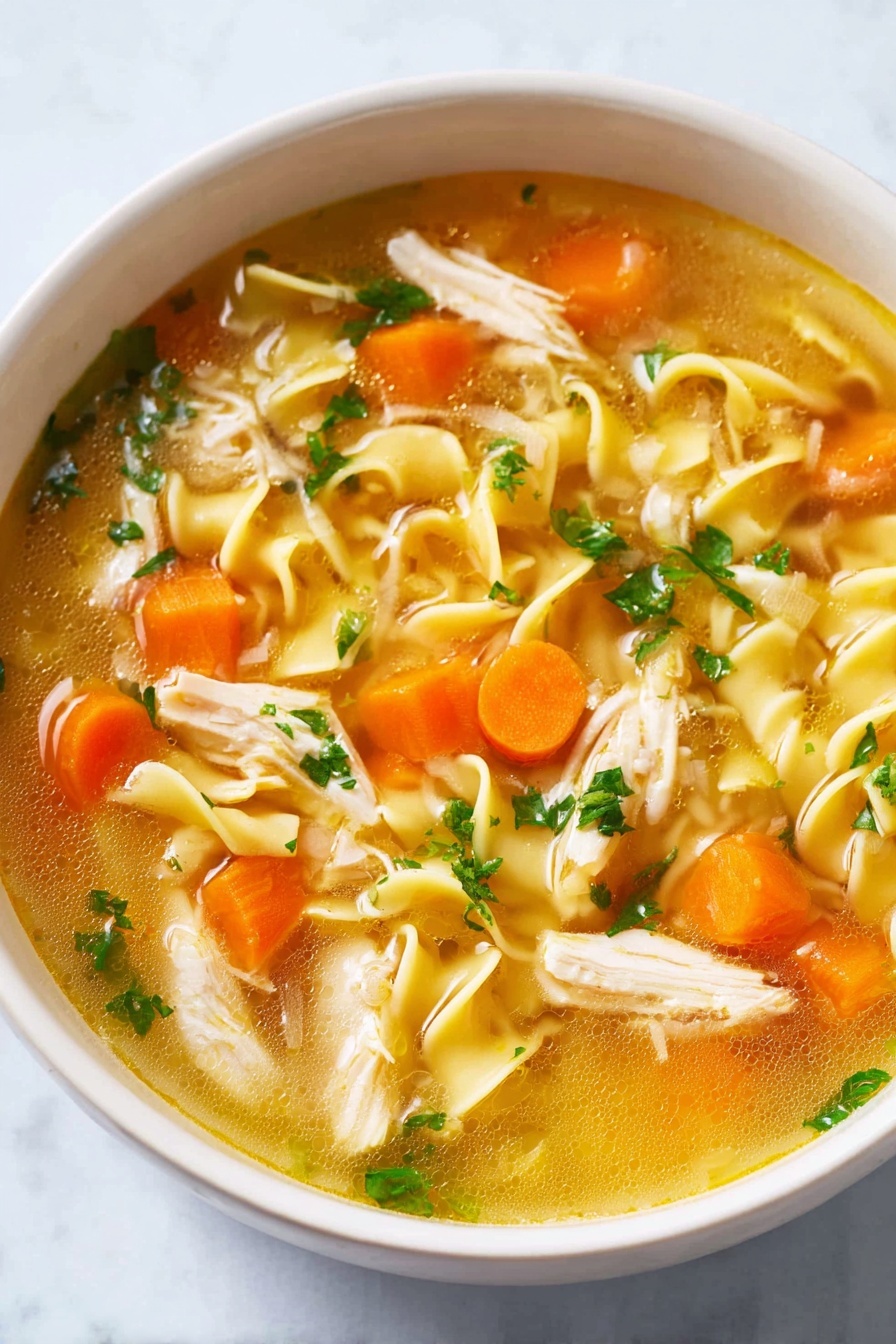 A white bowl filled with clear golden broth containing curly yellow noodles, bright orange carrot cubes, soft white onion pieces, light beige shredded chicken, and small green parsley leaves scattered on top, all resting on a white marbled surface photo taken with an iphone --ar 2:3 --v 7 - Homemade Chicken Noodle Soup, comforting chicken soup recipe, easy homemade chicken noodle soup, healthy chicken noodle soup, quick chicken noodle soup