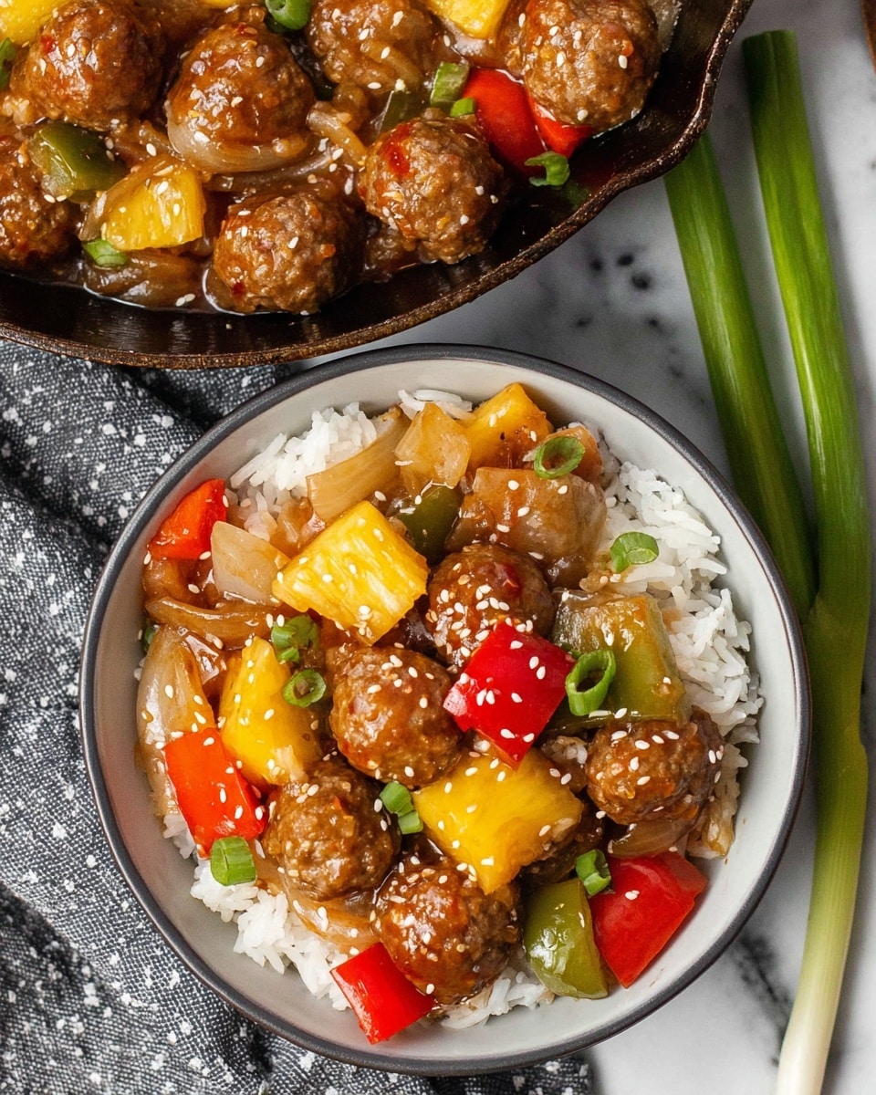 A white bowl filled with a base layer of fluffy white rice, topped with a colorful mix of small brown meatballs, bright yellow pineapple chunks, red and green bell pepper pieces, and translucent light brown cooked onions, all coated in a glossy brown sauce and sprinkled with white sesame seeds. The bowl sits on a white marbled surface beside a cast iron pan holding more of the same mix. Some green onions lie next to the bowl on a gray cloth with white dots. Photo taken with an iphone --ar 4:5 --v 7