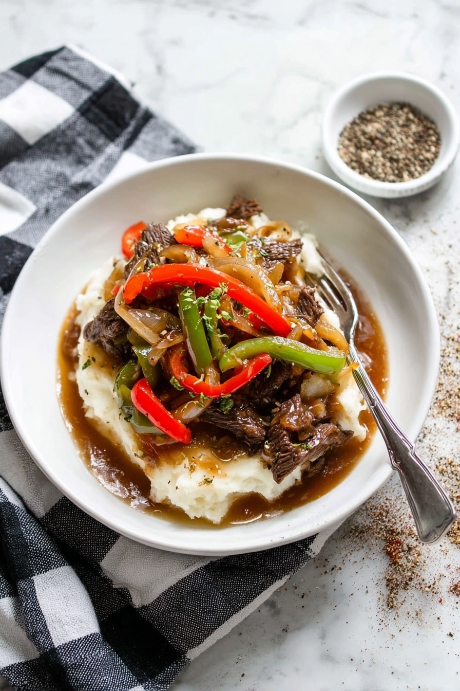 A white shallow bowl holds a layered dish with mashed potatoes at the bottom, creamy white and soft in texture. On top, there are strips of beef cooked dark brown, mixed with sautéed red and green bell pepper slices, and translucent cooked onions. The layers are covered with a glossy brown gravy that pools slightly at the base. A silver fork rests on the edge of the bowl. The bowl sits on a black and white checkered cloth, placed on a white marbled surface. To the top right, there is a small white dish with cracked black pepper scattered around it. photo taken with an iphone --ar 2:3 --v 7 - Pepper Steak with Onion, pepper steak recipe, savory steak with peppers, hearty beef stir-fry, easy beef and onion dinner
