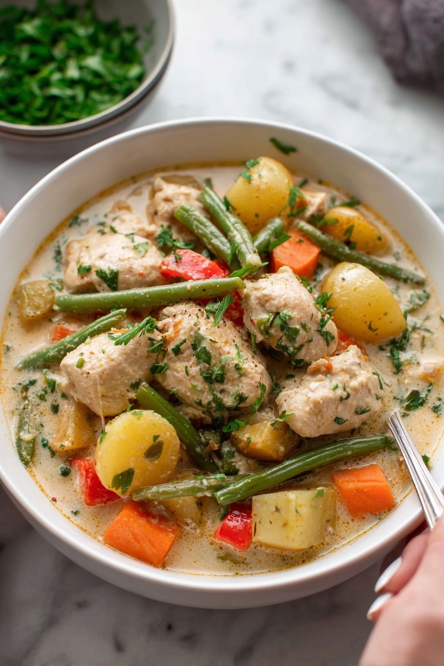 A white bowl filled with creamy chicken stew, showing large pieces of light brown chicken and chunky vegetables including orange carrots, green beans, yellow potatoes, and small bits of red pepper, all mixed in a thick, pale sauce with visible herbs on top; in the background, a bowl of chopped green herbs rests on a white marbled surface, and a woman's hand holding a spoon is partly visible at the bottom right. photo taken with an iphone --ar 2:3 --v 7 - Hearty Chicken and Root Vegetable Stew, comforting chicken stew with root vegetables, easy chicken and veggie stew, cozy chicken stew recipe, nourishing root vegetable stew
