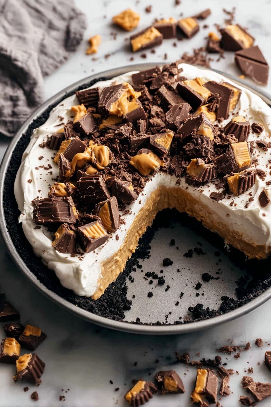 A round dessert in a gray pan has three layers: a dark crumbled base, a thick light brown peanut butter layer, and a smooth white cream layer on top. The cream is covered with many pieces of dark chocolate and peanut butter candy scattered unevenly. The pan is placed on a white marbled surface with more pieces of the same chocolate candy spread around it. A large wedge is missing from the dessert, showing the three colorful layers clearly. photo taken with an iphone --ar 2:3 --v 7 - Chocolate Peanut Butter Pie, Chocolate Peanut Butter Pie recipe, Easy Peanut Butter Pie, No-Bake Chocolate Pie, Creamy Chocolate Peanut Butter Dessert