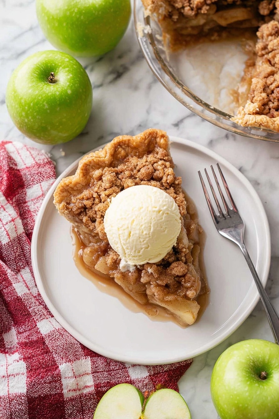 A white plate holds a single slice of apple crumble pie showing three visible layers: a golden brown crinkled crust on the outside edge, a thick middle layer of soft apple pieces coated in sticky brown sugar sauce, and a crumbly cinnamon topping in light and dark brown tones. On top of the pie slice sits a round scoop of creamy off-white vanilla ice cream that is starting to melt slightly. A silver fork lies diagonally on the plate pointing toward the bottom right corner. The plate rests on a white marbled surface surrounded by four whole shiny green apples and one apple cut in half showing pale yellow flesh inside. A red and white checkered cloth sits near the plate's bottom left corner. In the upper right corner, a glass pie dish contains the remaining apple crumble pie with a missing slice. Photo taken with an iphone --ar 2:3 --v 7 - Dutch Apple Pie, apple pie with crumb topping, homemade apple pie, cozy dessert recipes, classic apple pie