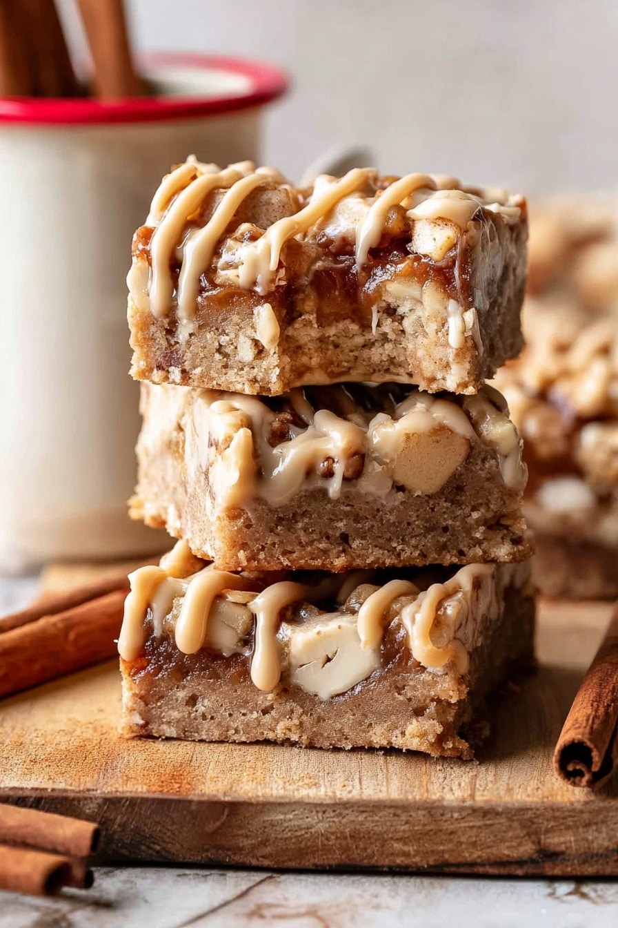 The image shows three square bars stacked vertically on a wooden surface with a single bite taken from the top bar. Each bar has a thick, crumbly base layer in light brown with small white nut pieces embedded inside. On top of the base, there is a layer of darker brown chunks with a soft texture, drizzled with thick, pale caramel-colored frosting in thin, uneven lines. A cinnamon stick is placed near the bottom left corner, and a white mug with a red rim and two cinnamon sticks inside is partially visible to the right. The background is a white marbled texture. Photo taken with an iphone --ar 2:3 --v 7 - Brown Butter Apple Blondies with Cinnamon Maple Glaze, fall dessert recipes, cozy apple blondies, cinnamon maple glaze treat, easy autumn blondies