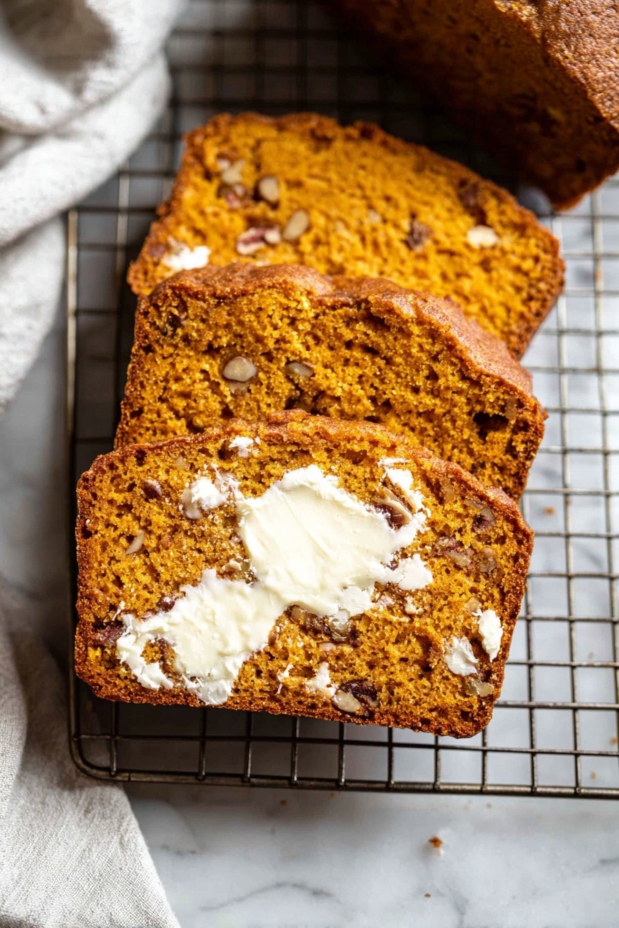 The image shows three thick slices of moist, orange-brown bread with small pieces of nuts inside, laid out on a metal cooling rack. The front slice is spread with melting white butter that contrasts with the bread’s warm color, showing a soft and slightly crumbly texture. The nuts inside the bread add darker brown spots throughout. The cooling rack is placed on a white marbled surface, and part of a white cloth is visible in the background. photo taken with an iphone --ar 2:3 --v 7 - Pumpkin Bread, Easy Pumpkin Bread, Fall Baking Recipes, Moist Pumpkin Bread, Spiced Pumpkin Bread