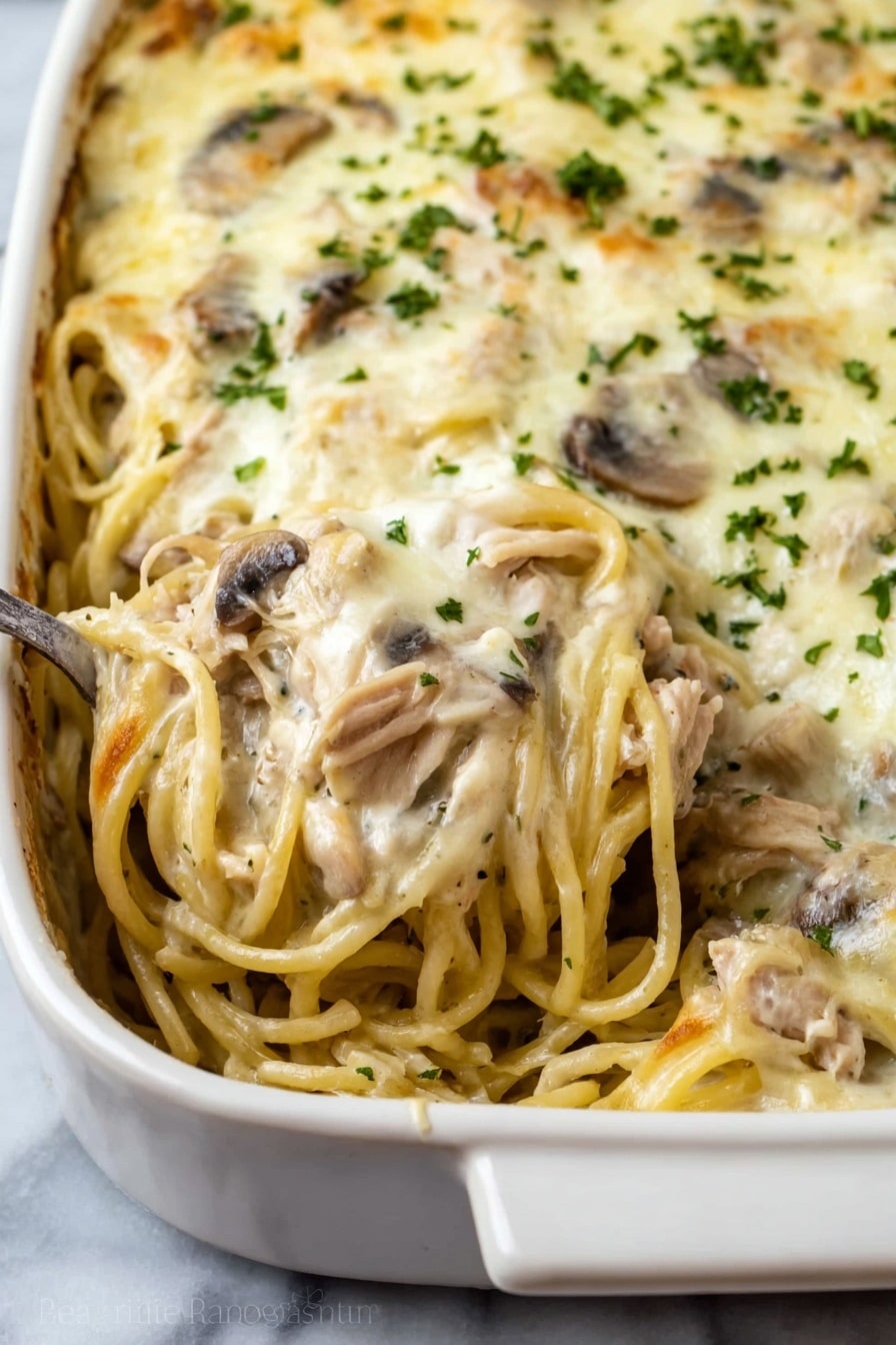 This dish shows a close-up view of a baked pasta casserole in a white ceramic dish. The casserole consists of creamy spaghetti mixed with pieces of light brown cooked meat and sliced mushrooms spread throughout. The top layer is covered with a smooth, melted white cheese sauce sprinkled with small bits of green herbs. A spoon is scooping some of the creamy pasta from the dish, showing the mixed layers of noodles, meat, and mushrooms inside. The dish is placed on a white marbled surface. photo taken with an iphone --ar 2:3 --v 7 - Creamy Chicken Tetrazzini Bake, easy chicken casserole, cheesy pasta bake, weeknight dinner ideas, comforting chicken bake