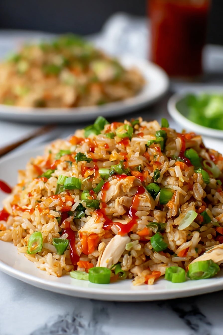 A close-up view of a white plate filled with fried rice, showing layers of light brown rice mixed with small pieces of white chicken, bright green chopped spring onions, and small orange-red peppers scattered throughout. The rice is lightly coated with red sauce drizzled on top, adding a glossy texture. In the background, there is a blurred white plate with more fried rice, placed on a white marbled surface. The overall colors are warm with green, red, and white contrasts. Photo taken with an iphone --ar 2:3 --v 7 - Quick Chicken Fried Rice, chicken fried rice, easy fried rice recipe, quick dinner ideas, homemade Asian fried rice