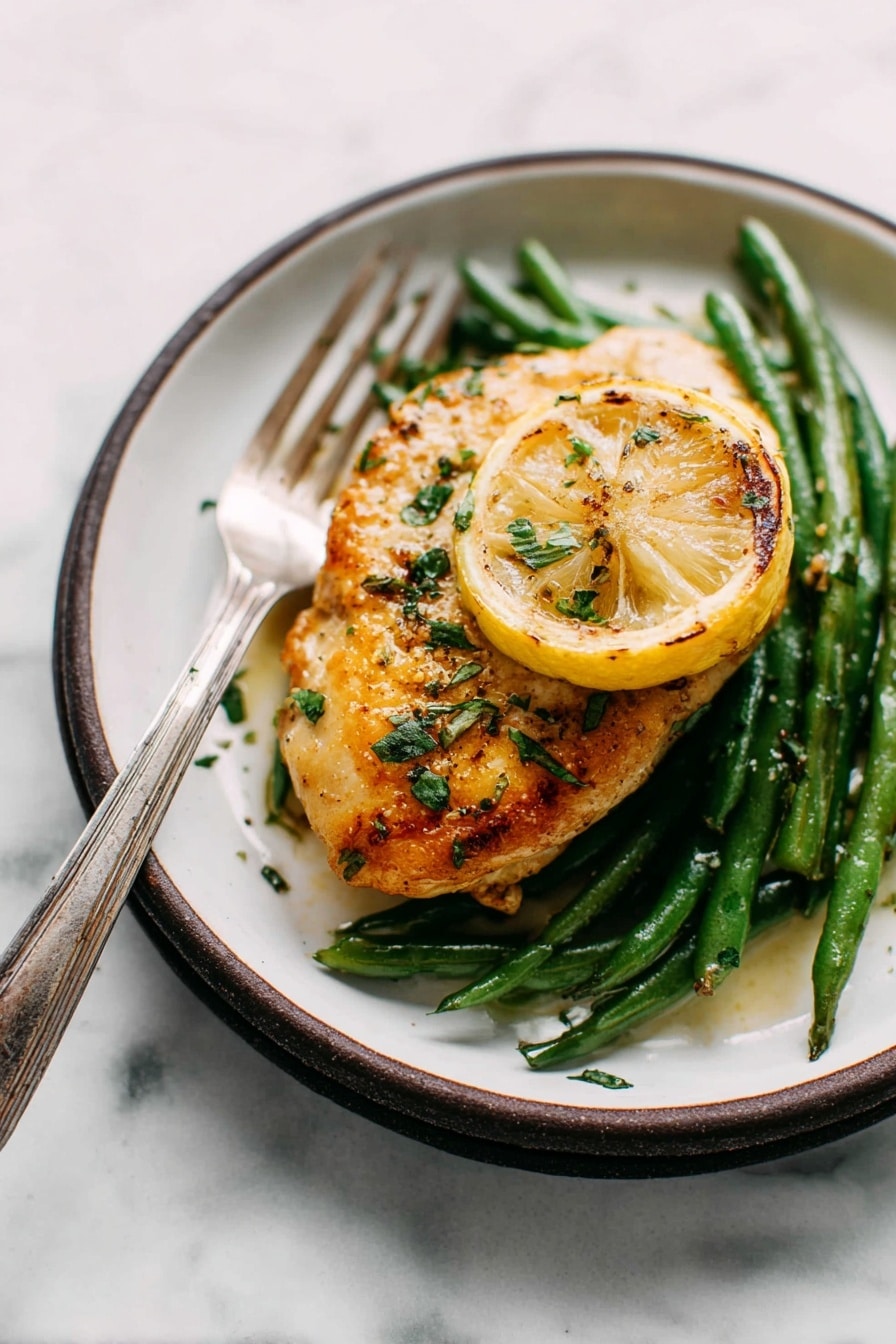 The image shows a single piece of golden-brown cooked chicken placed on top of a bed of green beans. Under the chicken, there is a slice of grilled lemon adding a pop of yellow color. The chicken is sprinkled with fresh green herbs and some seasoning that gives it a slightly glossy texture. The dish is served on a white plate with a dark rim, and a silver fork with an aged handle is resting on the edge of the plate. The surface beneath the plate has a white marbled texture, creating a clean and simple background. photo taken with an iphone --ar 2:3 --v 7 - Garlic Lemon Butter Chicken Skillet, easy chicken skillet recipe, one-pan chicken dinner, lemon garlic chicken, healthy chicken recipes