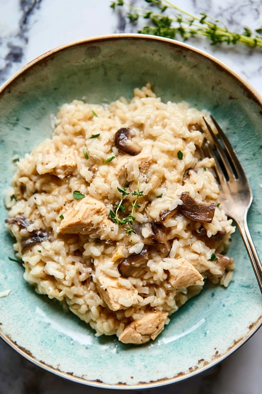 A textured turquoise bowl filled with creamy light beige risotto as the base layer, mixed with medium brown whole mushrooms and light tan chunks of chicken scattered evenly on top. A few sprigs of fresh green herbs sit on one side, adding a pop of color. The bowl rests on a white marbled surface with a folded dark grey cloth nearby, and a silver fork placed inside the bowl on the right side. The overall look is soft and earthy, with natural lighting enhancing the creamy texture of the dish photo taken with an iphone --ar 2:3 --v 7 - Creamy Chicken Mushroom Risotto, chicken mushroom risotto recipe, easy risotto recipes, comforting mushroom risotto, one-pan chicken risotto