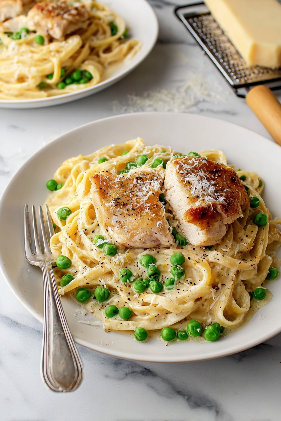 A white plate holds a creamy pasta dish with three slices of golden-brown grilled chicken placed on top. The pasta is mixed with bright green peas and coated in a smooth white sauce. Sprinkled parmesan cheese and black pepper garnish the dish. A spoon and fork rest on the left side of the plate. The plate sits on a white marbled surface, with a beige cloth napkin visible on the right side and a small piece of grated cheese and a grater partially seen toward the top right corner. photo taken with an iphone --ar 2:3 --v 7 - Turkey Alfredo Pasta, creamy turkey pasta, leftover turkey recipes, quick weeknight pasta, comforting turkey pasta