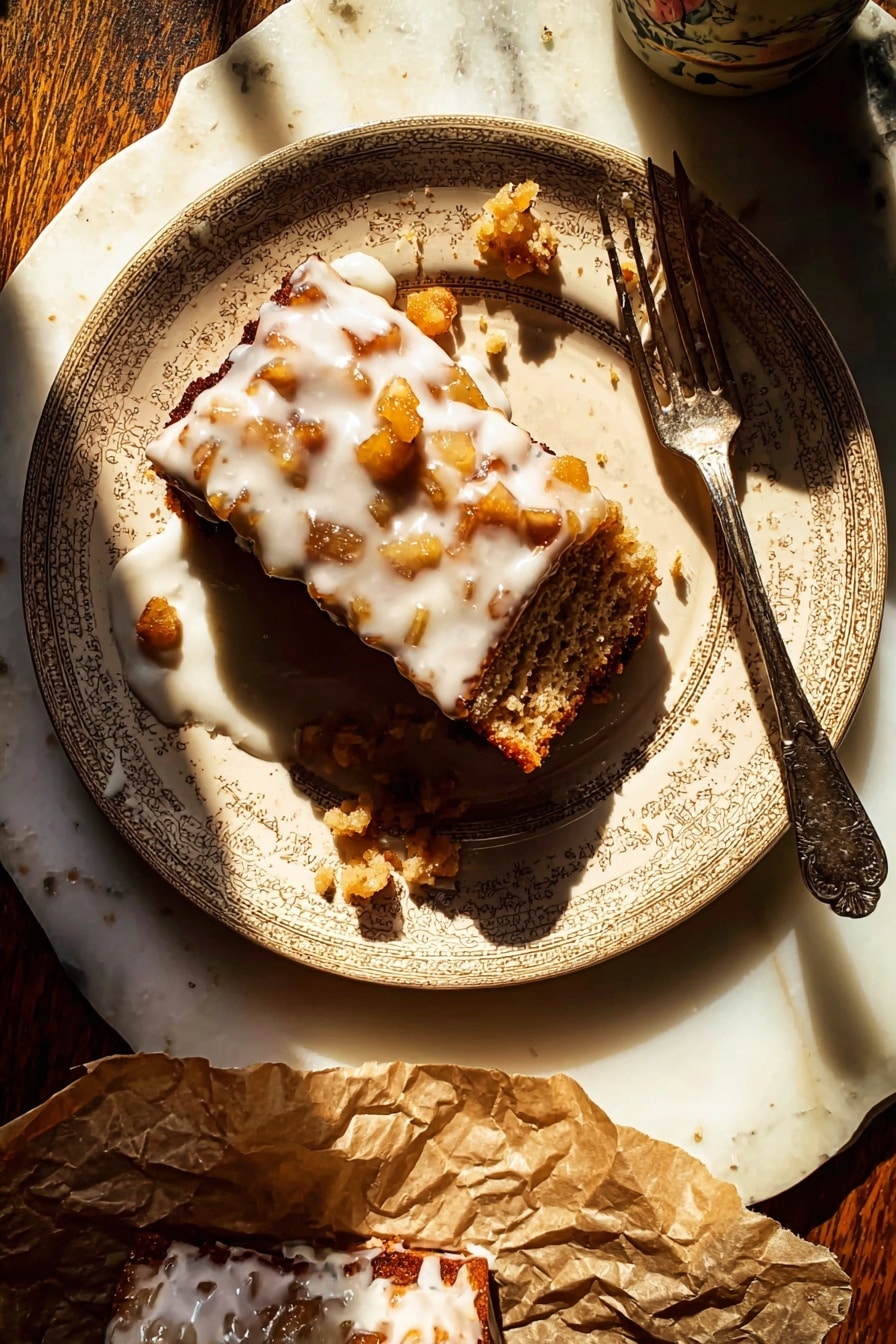 A beige patterned plate holds a rectangular piece of dessert with a rough brown base layer filled with small golden-brown chunks. The top layer is covered in a thick white glaze dripping down the sides and pooling slightly on the plate. There are small scattered bits of the dessert around the main piece, and an old-fashioned silver fork rests diagonally across the plate, partially touching the dessert. The plate sits on a white marbled surface, with sunlight casting strong shadows. A portion of the dessert is also on crumpled brown paper at the bottom of the image, also drizzled with white glaze. Photo taken with an iphone --ar 2:3 --v 7 - Glazed Honeycrisp Apple Fritter Cake, apple fritter cake, honeycrisp apple dessert, fall apple cake, cinnamon apple cake