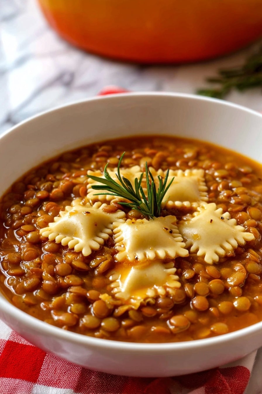 The image shows a white bowl filled with a thick vegetarian lentil soup layered with small, round brown lentils covering the entire surface, mixed with several square pieces of pale yellow pasta scattered evenly on top. The soup has a rich, brownish-orange broth giving the dish a warm color, with a small green rosemary sprig placed in the center as a garnish. The bowl rests on a red and white checkered cloth with a white marbled surface below, and a blurred background hinting at an orange pot. Photo taken with an iphone --ar 2:3 --v 7 - Umbrian Lentil Soup with Pasta, Italian lentil soup recipe, hearty Italian soup, rustic Umbrian cuisine, easy lentil soup with pasta