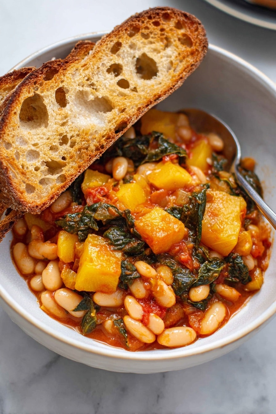 A white bowl filled with two thick slices of toasted bread resting on the left side, showing their golden-brown crispy texture with some holes and rough edges. The main part of the bowl is filled with a colorful mix of cooked white beans, yellow chunks of squash, and dark green leafy vegetables, all coated in a rich, slightly shiny red-orange sauce. The ingredients are close together, showing a hearty, rustic stew. A silver spoon is partially visible on the right side of the bowl, touching the food. The bowl sits on a white marbled surface. photo taken with an iphone --ar 2:3 --v 7 - Stewed Great Northern Beans with Kale, Tomatoes, and Herbs, healthy bean and kale stew, hearty vegetarian dinner, easy bean recipes, plant-based comfort food
