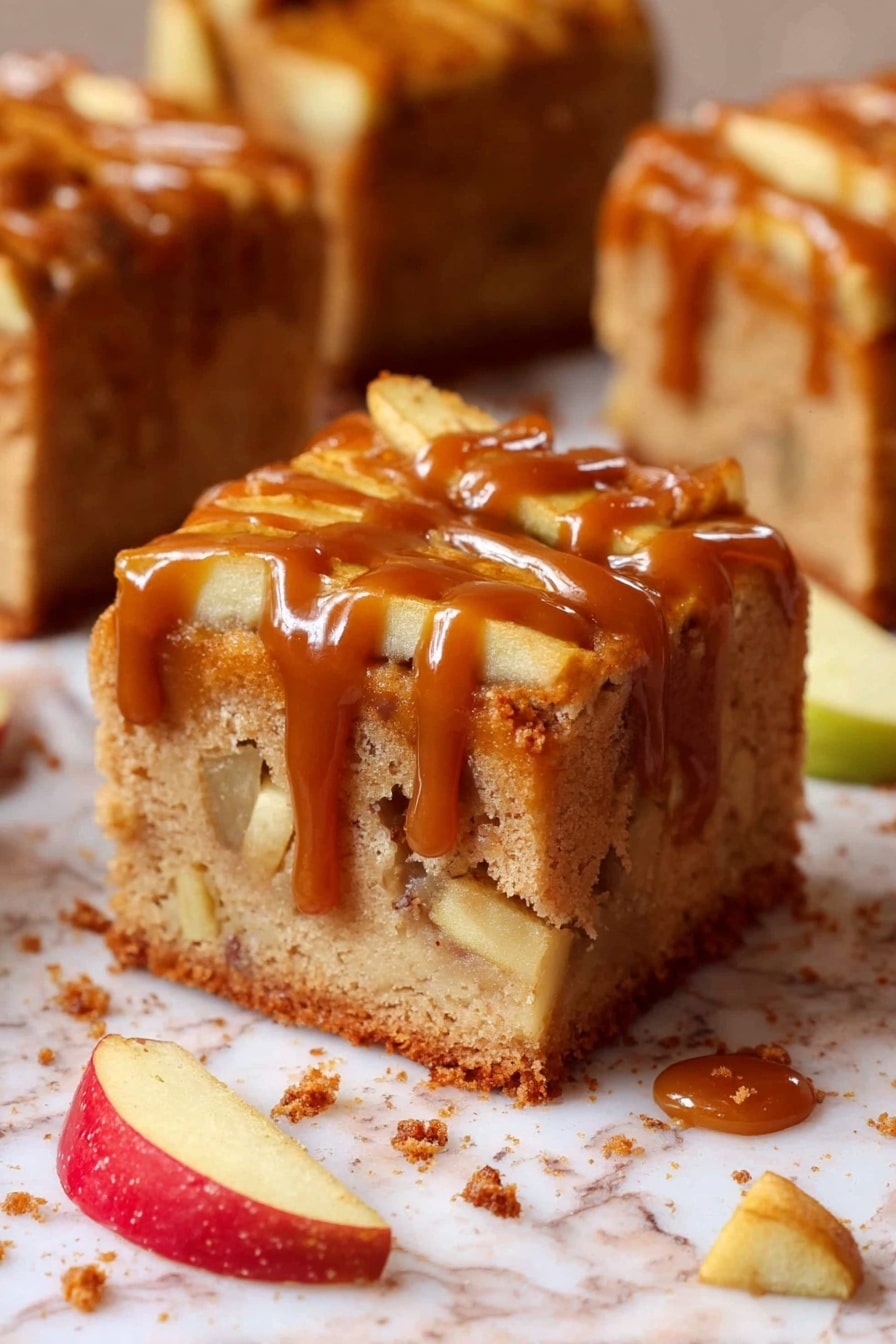 A thick square slice of apple cake shows two visible layers: the bottom is a light brown soft cake base with apple chunks inside, and the top layer is covered with thin apple slices partially lengthened by a messy layer of glossy caramel sauce dripping down the sides. The cake sits on white marbled surface sprinkled with crumbs, small apple chunks, and thin apple slices nearby. The background shows more similar cake slices out of focus. Photo taken with an iphone --ar 2:3 --v 7 - Caramel Apple Cake, fall dessert recipes, apple cake with caramel, cozy autumn desserts, easy apple cake recipe