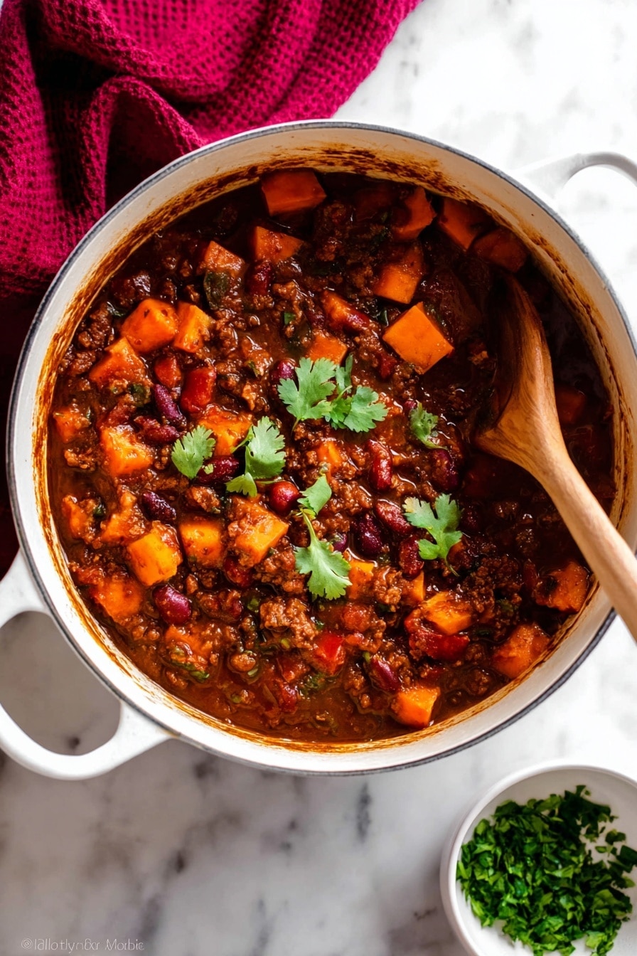 A white pot filled with thick stew that has three main layers: a dark brown sauce base, chunky orange sweet potato pieces, and visible red and brown beans mixed with ground meat; a few green cilantro leaves float on top near the center for color contrast. A wooden spoon is partially dipped on the right side, stirring the stew, showing the dense texture and rich sauce coating all ingredients. The pot rests on a white marbled surface with a dark red cloth draped in the upper left corner and a small white bowl filled with chopped green herbs placed near the bottom right. Photo taken with an iphone --ar 2:3 --v 7 - Vegetarian Pumpkin Chili, hearty pumpkin chili, healthy vegetarian chili, easy pumpkin chili recipe, cozy fall chili