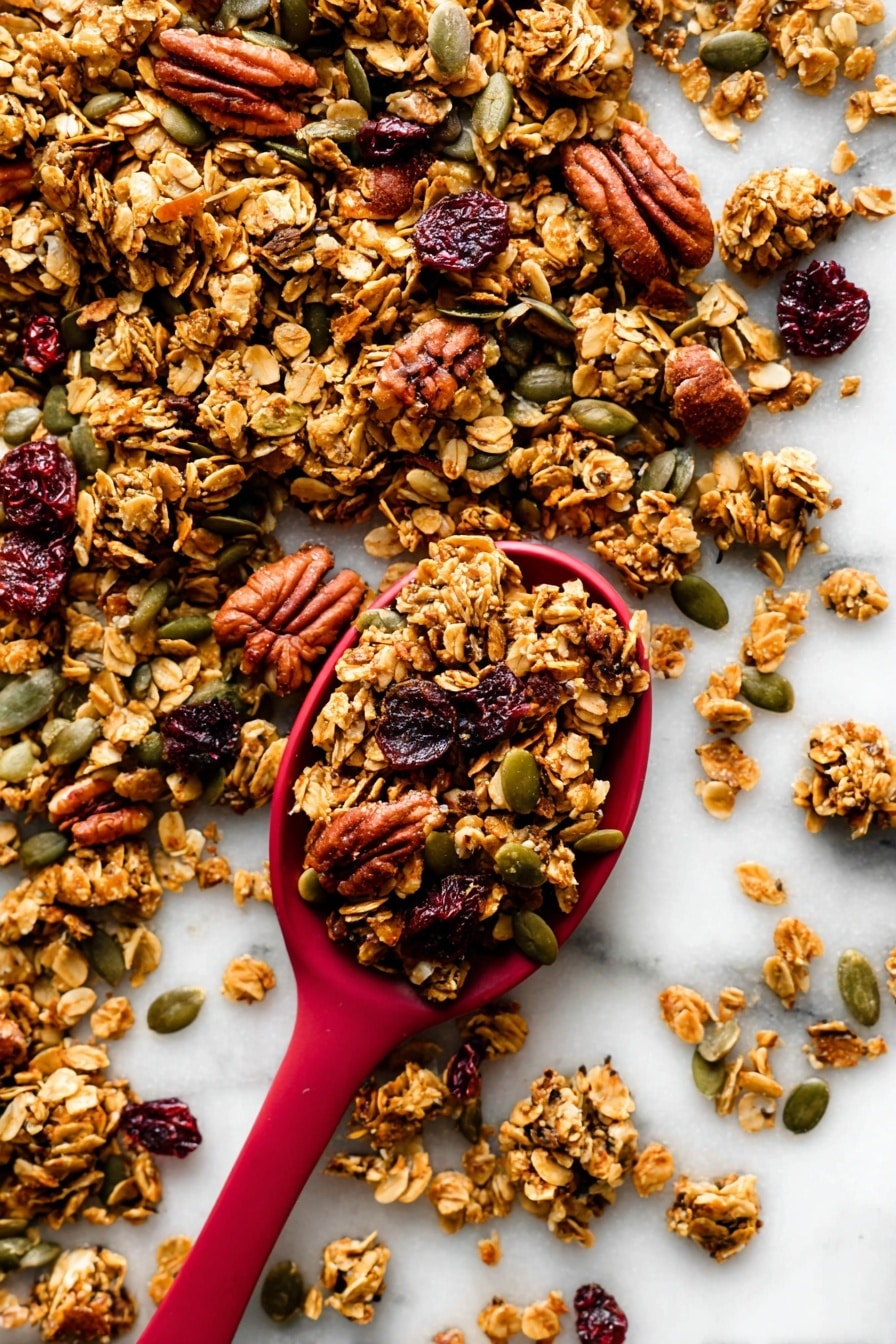 The image shows a close-up of crunchy granola scattered on a white marbled surface with a red spoon filled with granola placed near the center. The granola is made of golden-brown toasted oat clusters mixed with darker brown pecans, green pumpkin seeds, and dark red dried cranberries. The textures vary from rough and chunky oats and nuts to smooth seeds, creating a rich and inviting look. The red spoon contrasts strongly with the white background and the natural colors of the granola around it. photo taken with an iphone --ar 2:3 --v 7 - Pumpkin Spice Granola, fall granola recipe, cozy breakfast, crunchy pumpkin granola, healthy autumn snack
